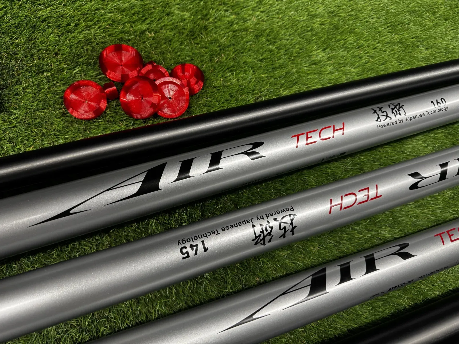 Daiwa Air Tech pole sections on grass beside a set of red Fox Worx pole bungs